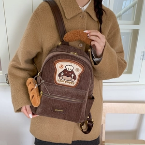 Detail view of brown corduroy backpack featuring chef puppy embroidery and plush baguette charm