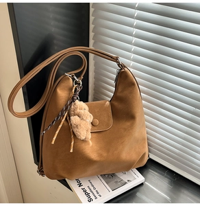 Brown suede tote bag detail with magnetic flap and cute plush bear charm on white magazine