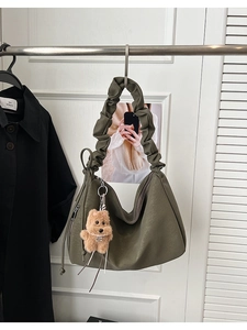 Detail of olive green hobo bag with cloud-pleated handle and brown plush bear charm