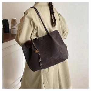 Detail view of deep brown suede tote bag with plush charm on model shoulder
