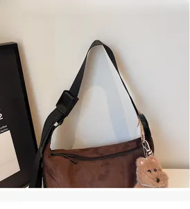 Detail of brown faux suede bag with black adjustable strap and plush bear charm