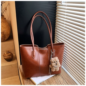 Detail of caramel faux leather tote bag with plush dog charm on wooden surface