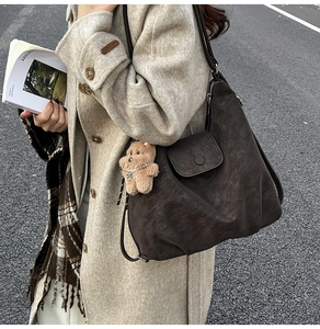 Detail of dark brown vintage tote bag with flip cover and cute plush bear charm