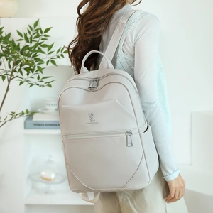 Detail view of cream pebble leather backpack featuring polished metal rabbit logo and zipper