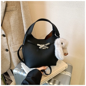 Detail of black leather bucket bag featuring silver bow clasp and plush rabbit charm