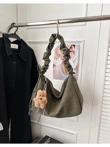 Detailed view of olive green tote bag featuring ruched strap and brown bear charm
