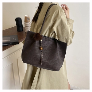 Detail of dark brown matte leather tote bag with plush charm and woven bell pendant