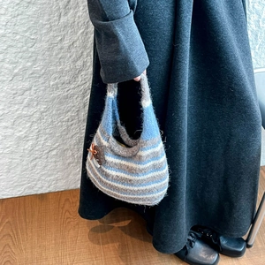 Detail of hand-woven striped crochet bucket bag featuring a decorative acorn charm