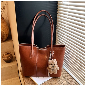 Detail of brown leather tote bag featuring contrast stitching and a cute puppy charm