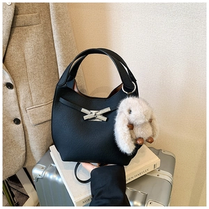 Close-up of black lychee leather bucket bag with silver bow buckle and rabbit plush toy