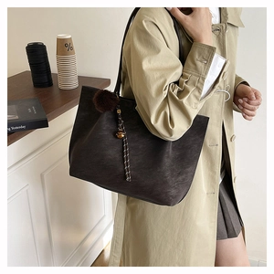 Detail of dark brown matte tote bag with fuzzy pompom charm and braided rope accent