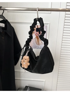 Detail of black crescent shoulder bag featuring a unique gathered pleated handle and bear charm