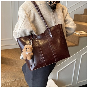 Detail of dark brown faux leather tote bag with cute plush bear charm on model shoulder