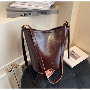 Detail of dark brown polished leather bucket bag with embossed fashion logo and adjustable strap