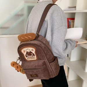 Detail of dark brown corduroy backpack with chef puppy embroidery and plush charm