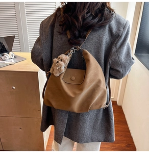 Brown suede tote bag shown on model featuring a decorative plush dog charm and flap closure
