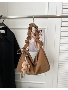 Close-up of brown pleated handle hobo bag featuring a cute plush dog charm accessory