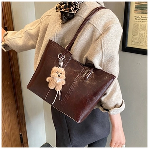 Detail of dark brown faux leather tote bag with plush bear charm and glossy finish