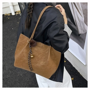 Brown vintage tote bag with decorative pompom and bell charm shown in a street style view
