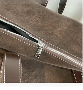 Detail of smooth silver zipper and stitching on brown vintage textured leather tote bag