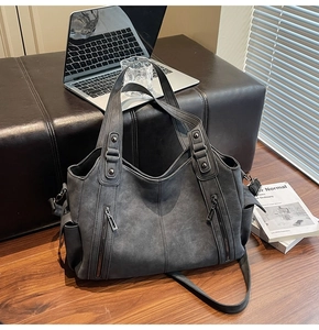 Detail view of large dark grey tote bag with zippers on a leather seat next to a laptop