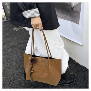 Brown suede tote bag with fur ball charm shown in a high-fashion street style view