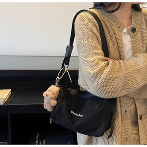 Detail of black canvas shoulder bag with white lettering and a plush dog charm pendant