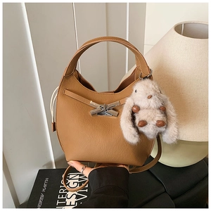 Close-up of camel leather bucket bag with metal buckle and soft plush rabbit charm