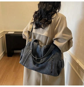 Detail of a grey matte leather tote bag with side pocket shown on a model