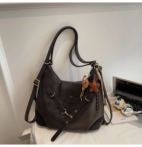 Detail of dark brown vintage faux leather tote with plush bear and star charms on desk