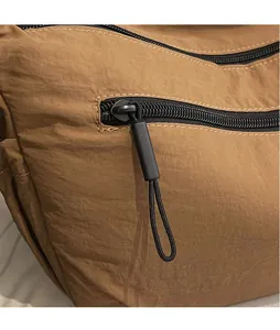 Detailed macro view of the black zipper and extended knot puller on a brown nylon bag