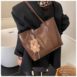 Detail of dark brown glossy PU leather tote bag with a cute plush teddy bear charm
