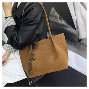 Close-up of brown suede tote bag with decorative pompom and metal bell charm detail