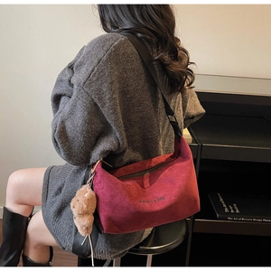 Detail of burgundy suede tote bag featuring adjustable strap and plush bear charm