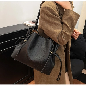 Detail of black ostrich-embossed bucket bag with gold metal rings and side drawstring