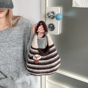 Detail of hand-knitted tote bag with striped pattern, mushroom badge, and leather bow