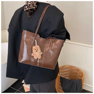 Detail of dark brown tote bag with glossy finish and cute plush bear charm on shoulder