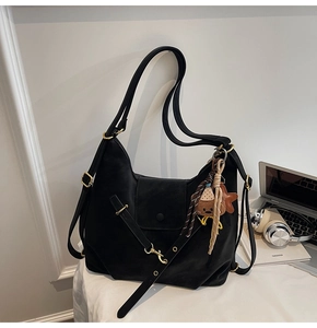 Detail of black large capacity hobo bag with gold hardware and bear charm on desk