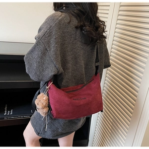 Model wearing a burgundy suede half-moon crossbody bag with a cute bear charm accessory