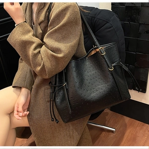 Detail of black ostrich embossed tote bag with decorative side drawstring and gold buckle