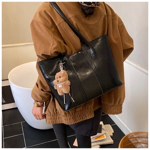Close-up of black PU leather tote bag with decorative stitching and a cute bear charm