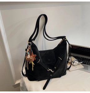 Detailed view of black matte leather tote bag with plush bear charm and metallic buckles
