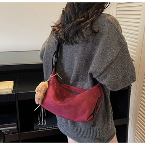 Detail of burgundy suede hobo bag with wide strap and cute plush bear charm