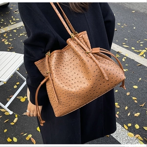 Detail of a brown ostrich embossed leather bucket bag with drawstring closure on a shoulder