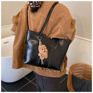 Detail of black glossy leather tote bag featuring a cute brown plush bear charm accessory