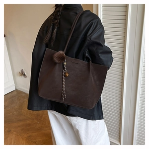 Detail view of large coffee brown suede tote bag with decorative plush ball and bell charm