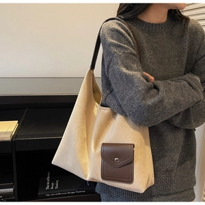 Dettaglio di una grande borsa tote beige con tasca in pelle marrone e fibbia in metallo