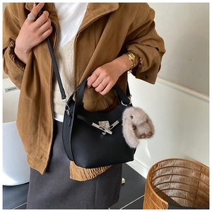 Detail of a black pebbled leather bucket bag featuring a silver clasp and plush rabbit charm