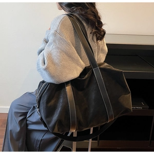 Detail of black large capacity shoulder bag with white contrast stitching on leather straps