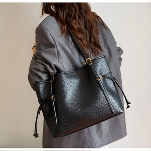 Detail of black ostrich-embossed tote bag featuring gold hardware and drawstring